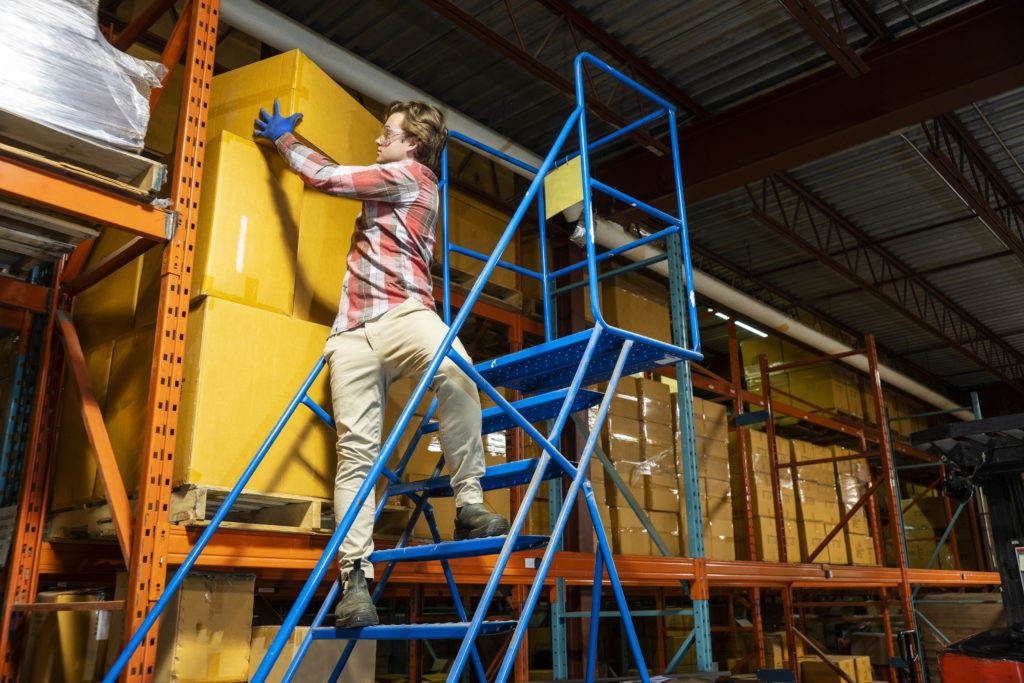 A male warehouse worker climbs a rolling ladder incorrectly.